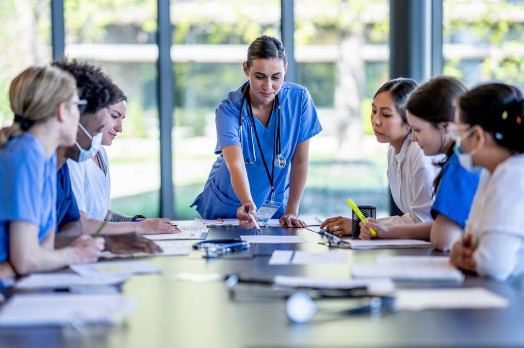 A group of pharma employees gather around a boardroom table with their team leader